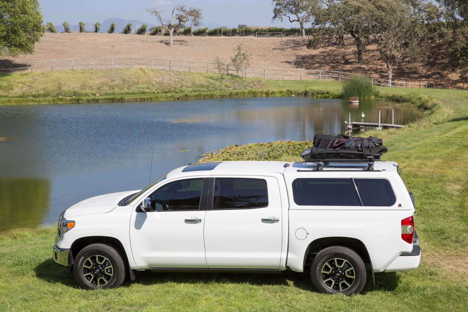 A white truck with a canopy on top of it is parked in front of a lake.