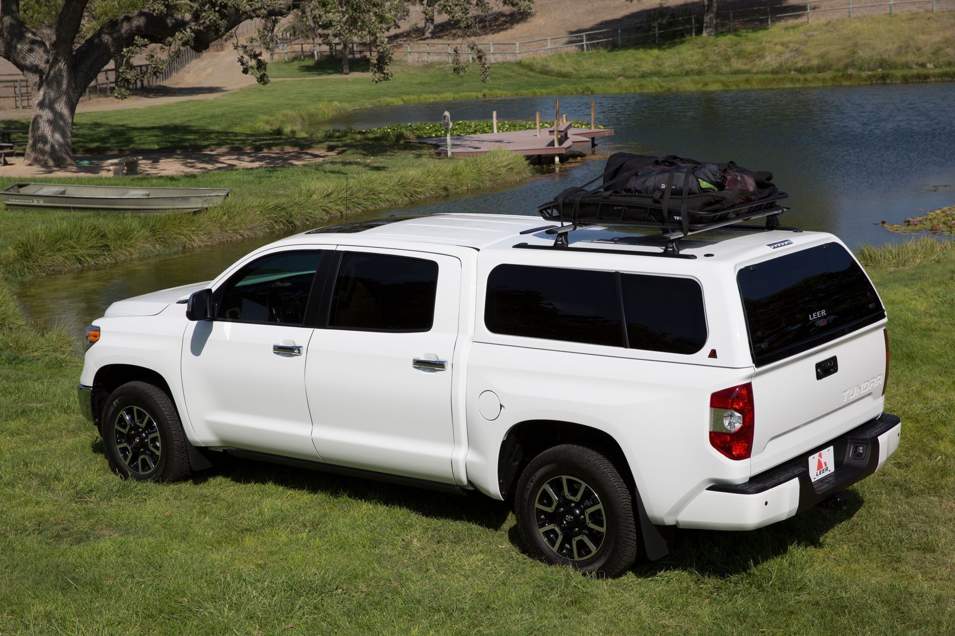A white truck with a canopy on top of it is parked in a grassy field.