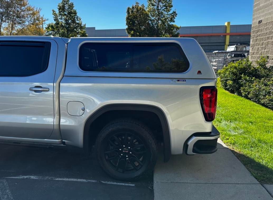 A silver truck with a canopy on top of it is parked on a sidewalk.