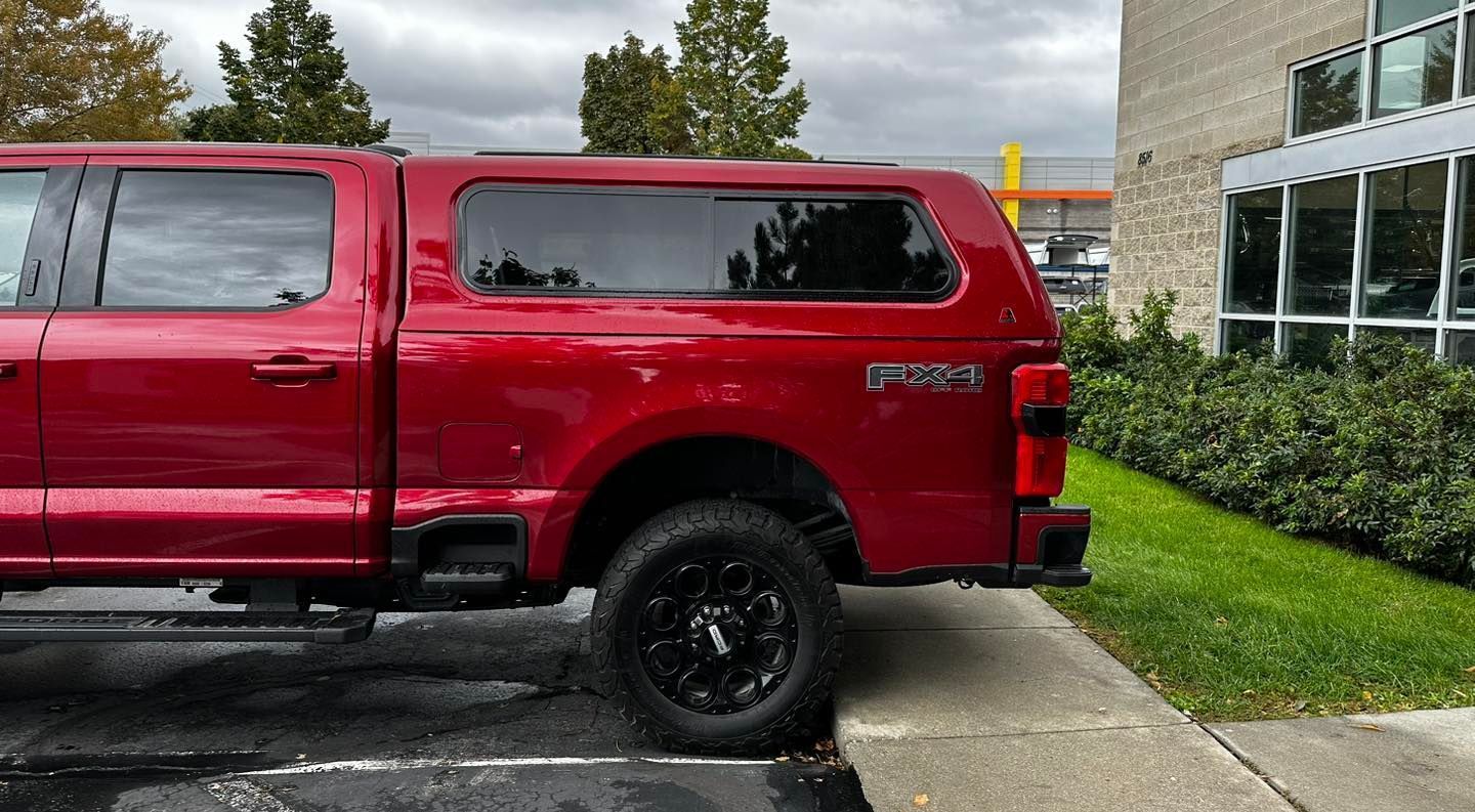 A red truck is parked in a parking lot next to a building.