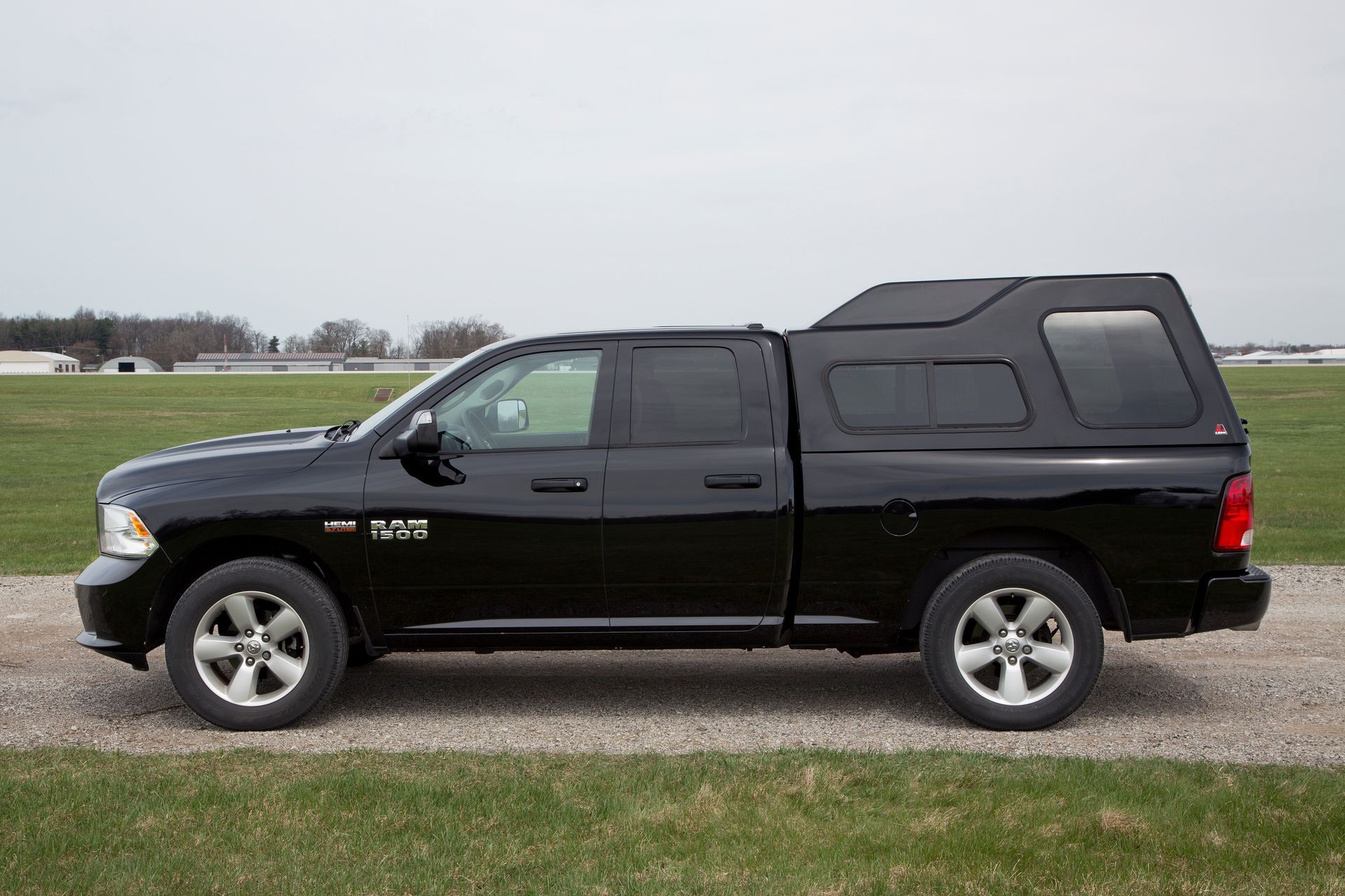 A black truck with a canopy on top of it is parked on a gravel road.