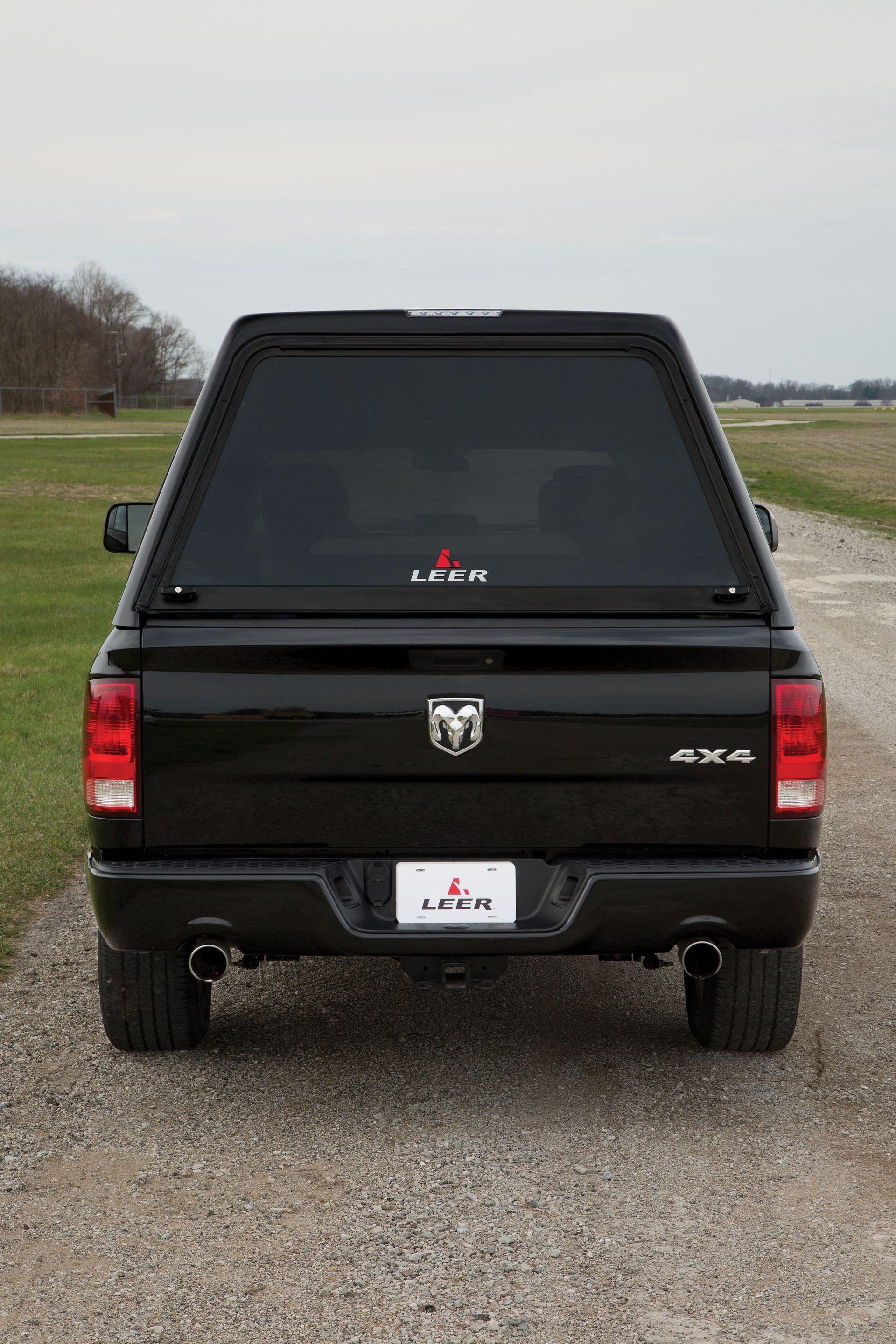 The back of a black truck with a bed cover is parked on a gravel road.