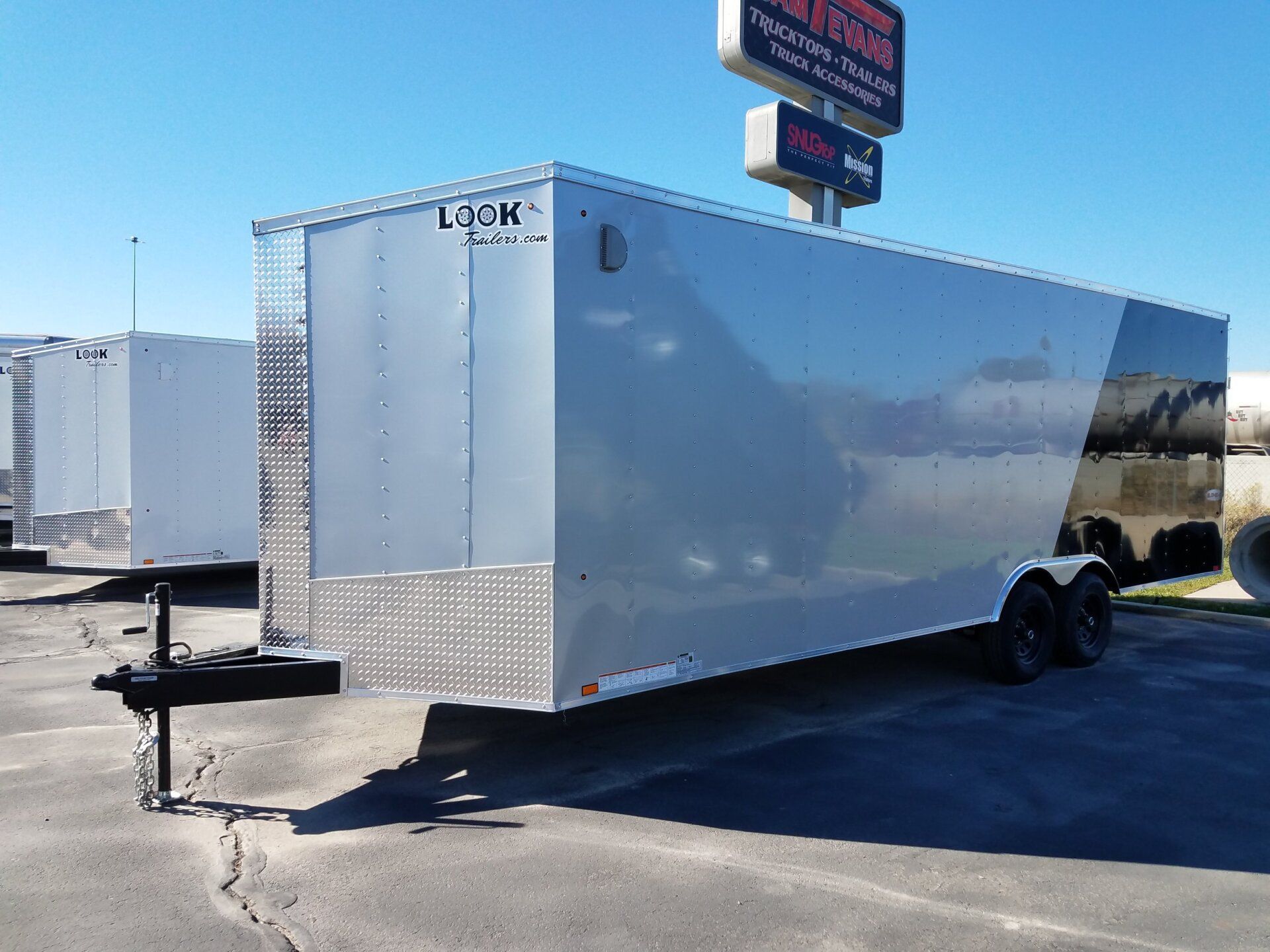 A silver trailer is parked in a parking lot with a sign above it.