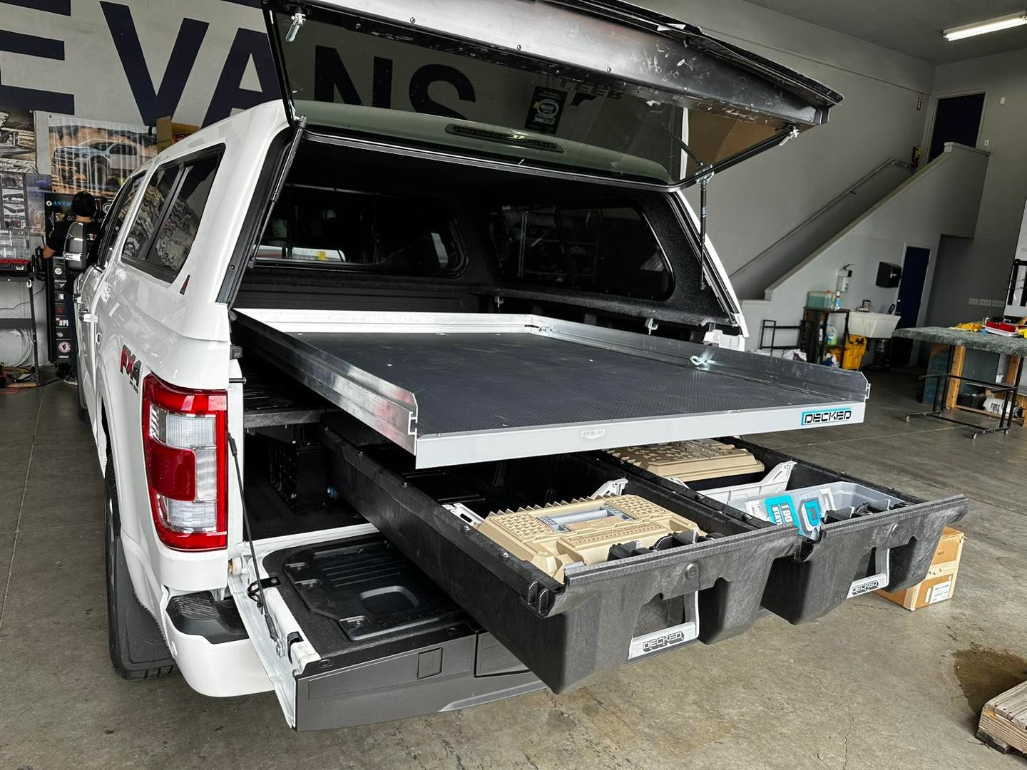 A white truck with a canopy and drawers in the back is parked in a garage.