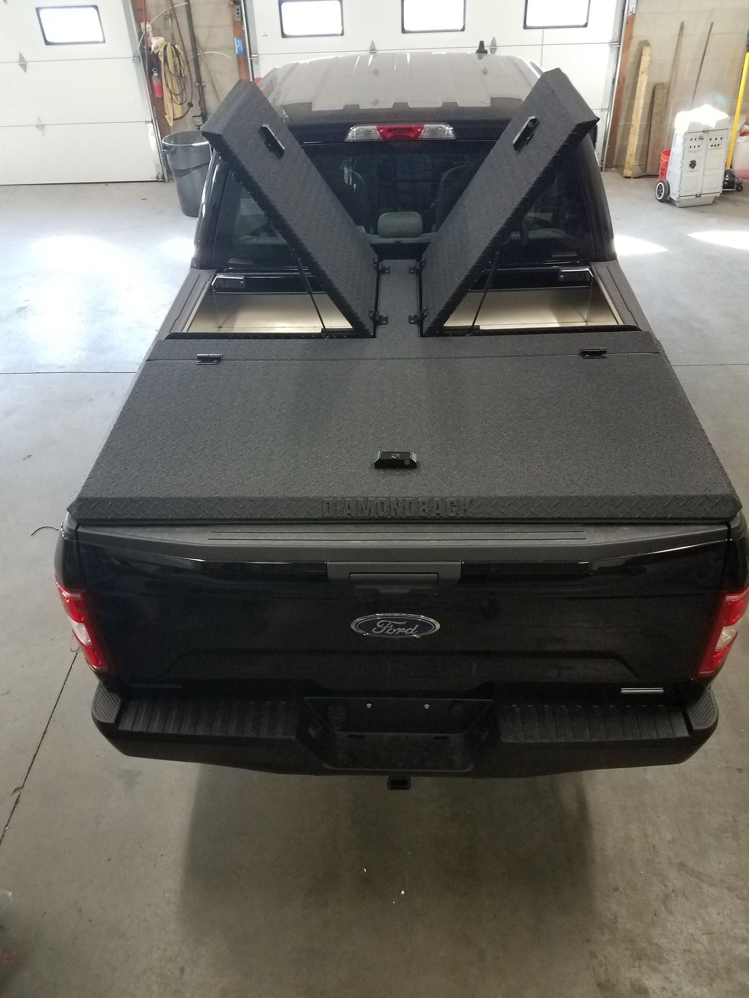 A black ford truck with its bed cover open in a garage.