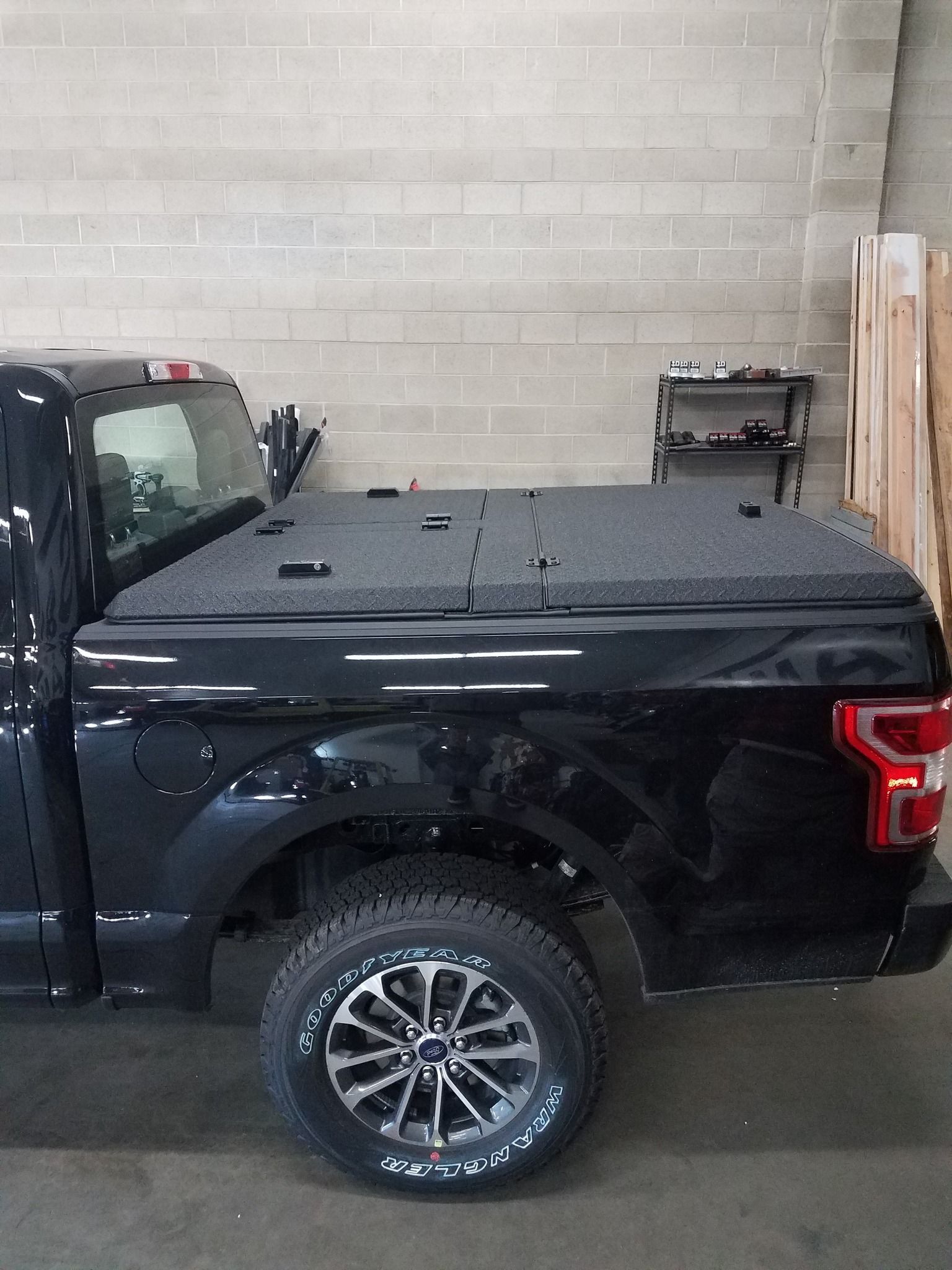 A black truck with a bed cover on it is parked in a garage.