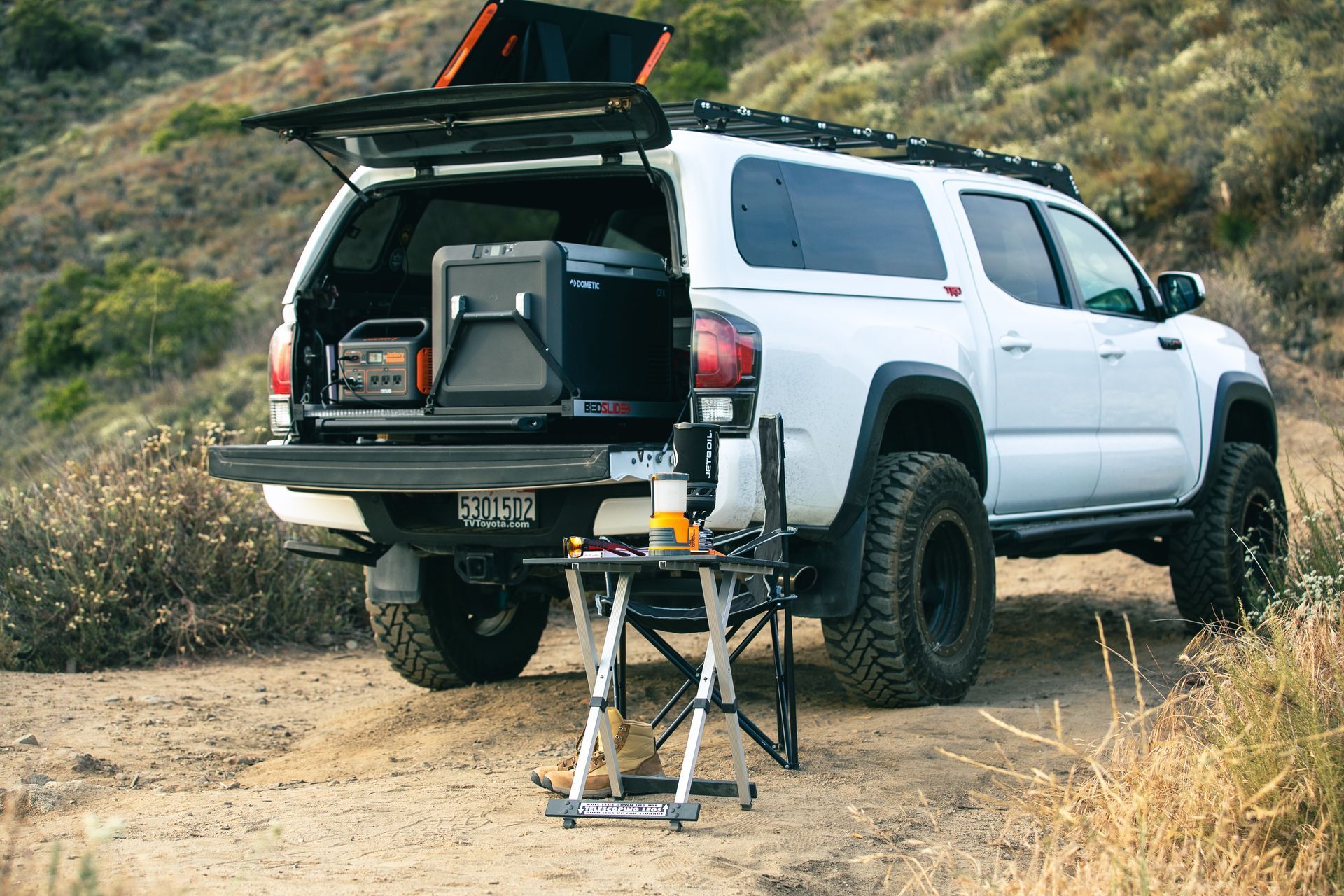 A white truck with the trunk open is parked on a dirt road.