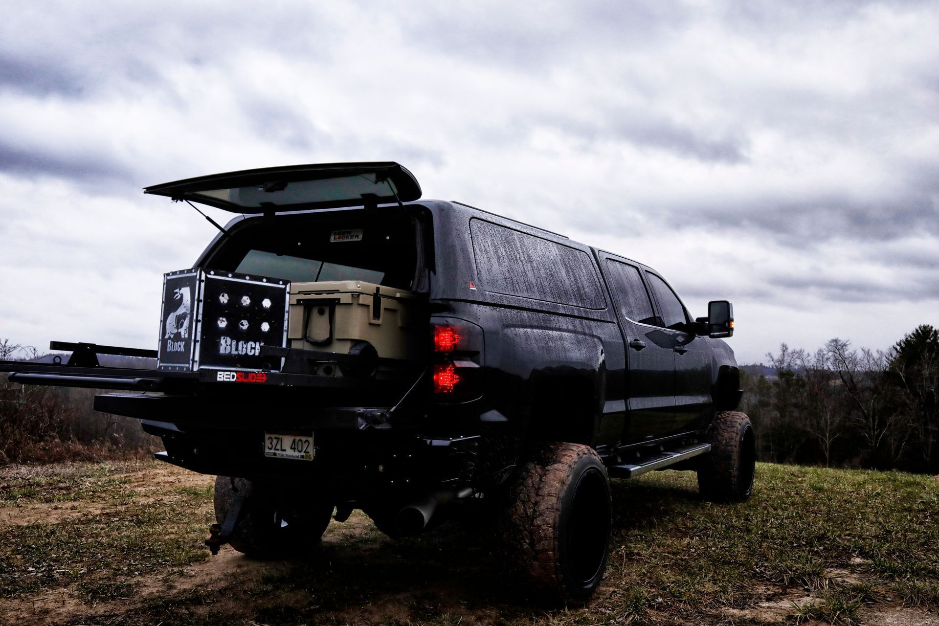 A black truck with the trunk open is parked in a grassy field.