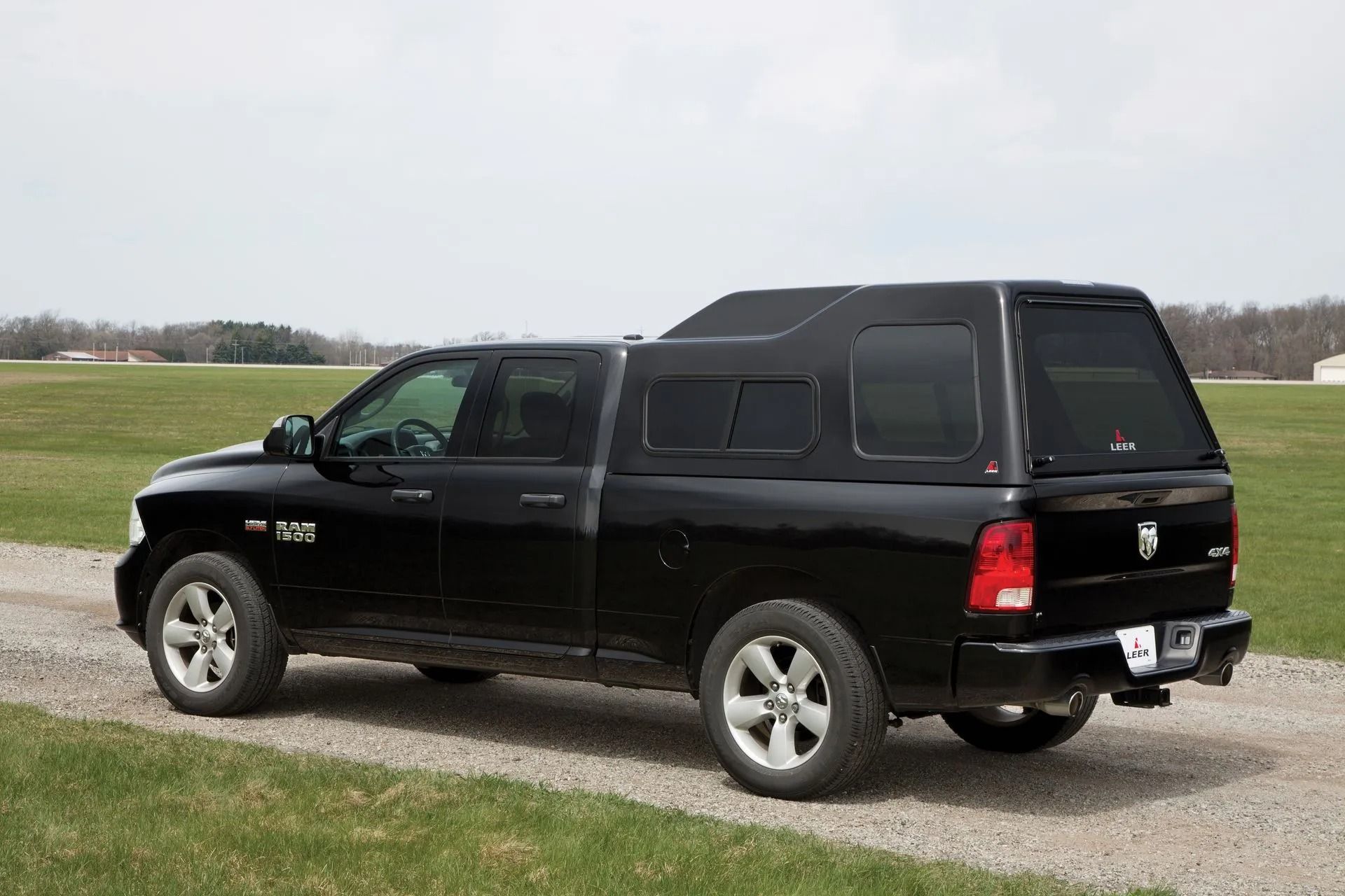 A black truck with a canopy on top of it is parked on a gravel road.