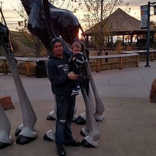 A man is holding a baby in front of a statue of a giraffe.