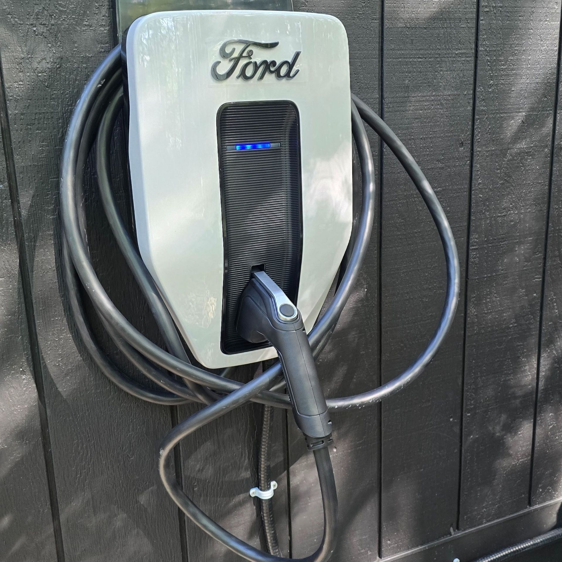 MJS Electrical Services - Electrician uses a multimeter to check wiring in a panel next to a white EV charger on a wall.