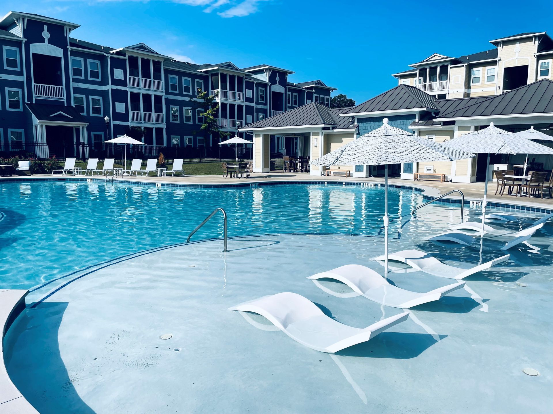 A large swimming pool with chairs and umbrellas in front of a building at Thomaston Crossing.