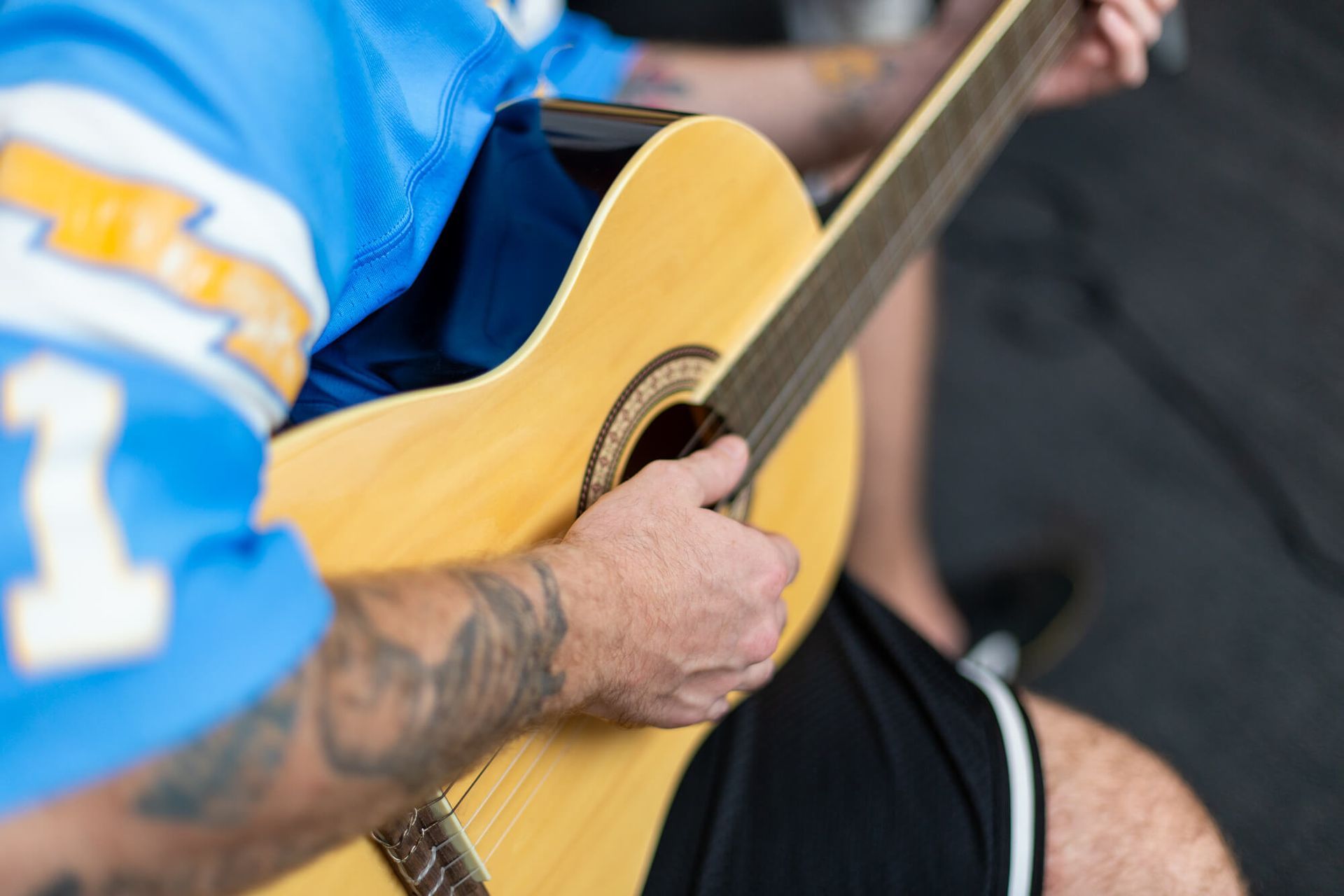 A man in a blue jersey is playing an acoustic guitar.