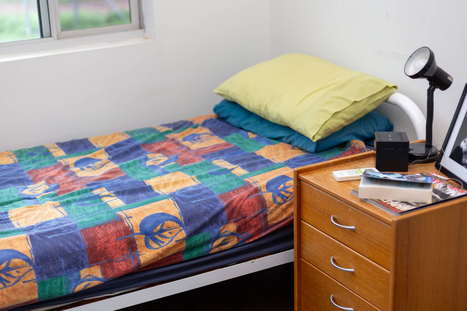 A bed with a colorful blanket is next to a nightstand.
