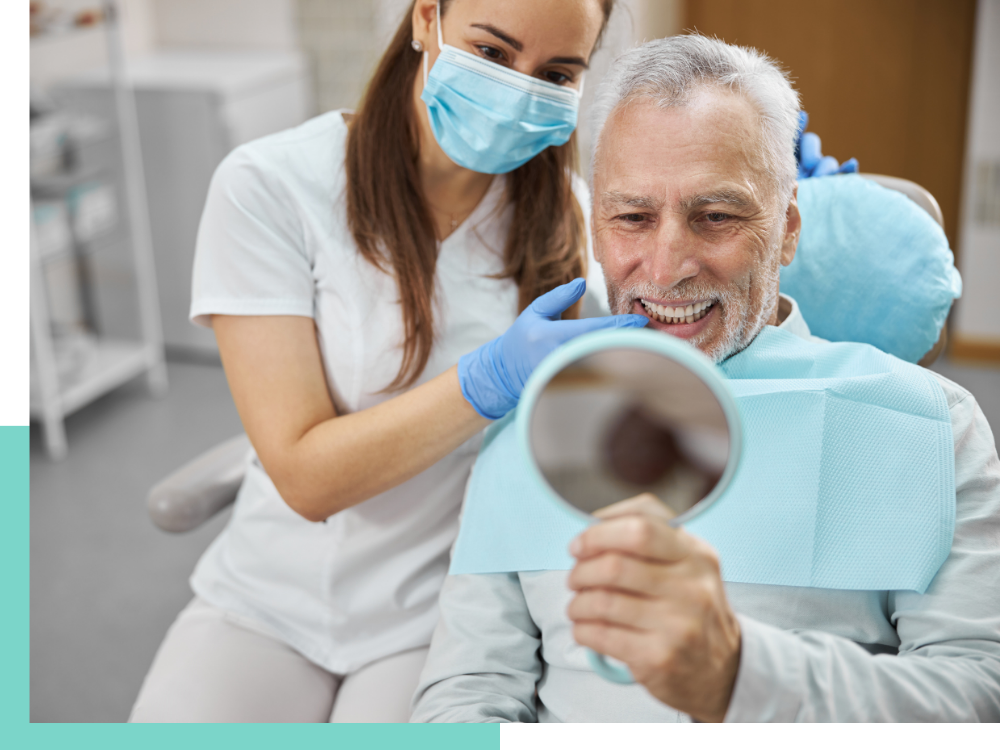 A photo of a senior man looking at his new smile in a mirror with a dental assistant