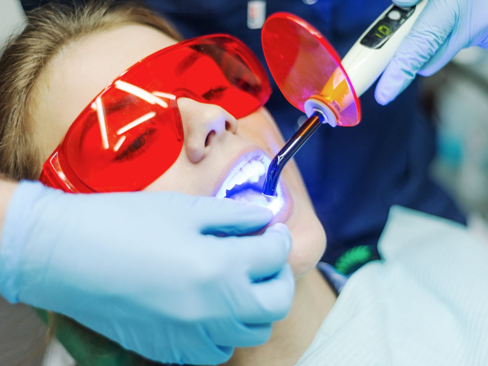 A woman wearing red goggles is getting her teeth whitened by a dentist.