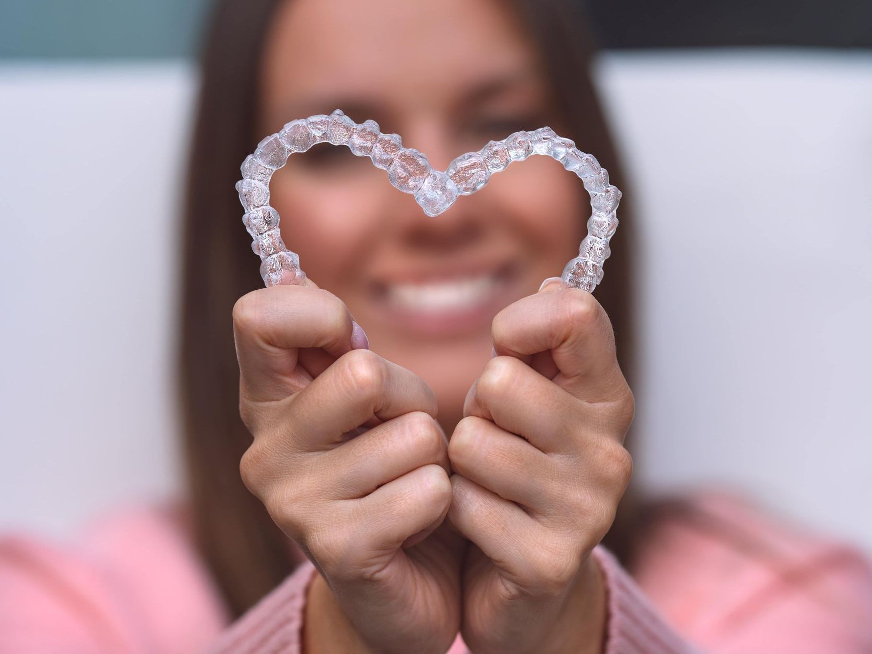 An image of a young woman holding two clear aligner trays