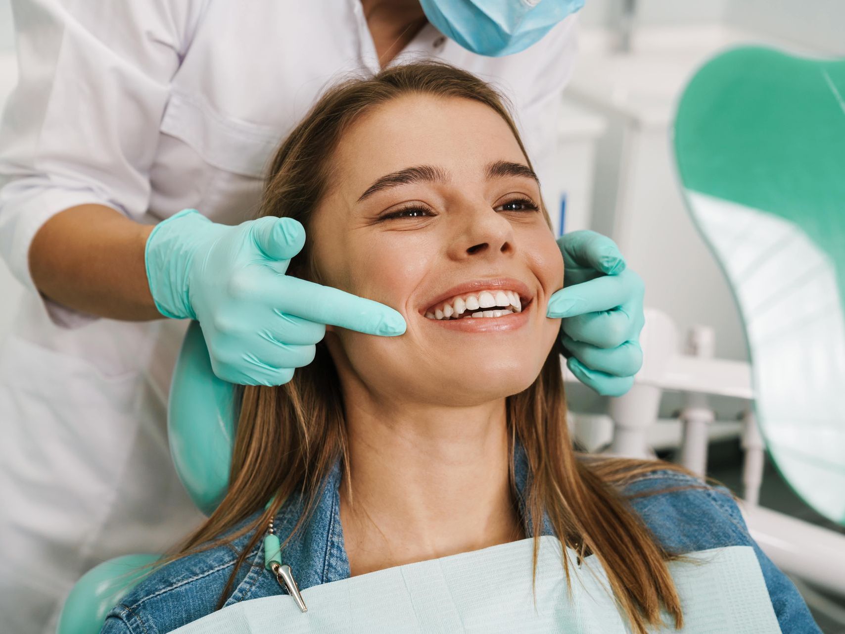 A woman is sitting in a dental chair while a dentist examines her teeth