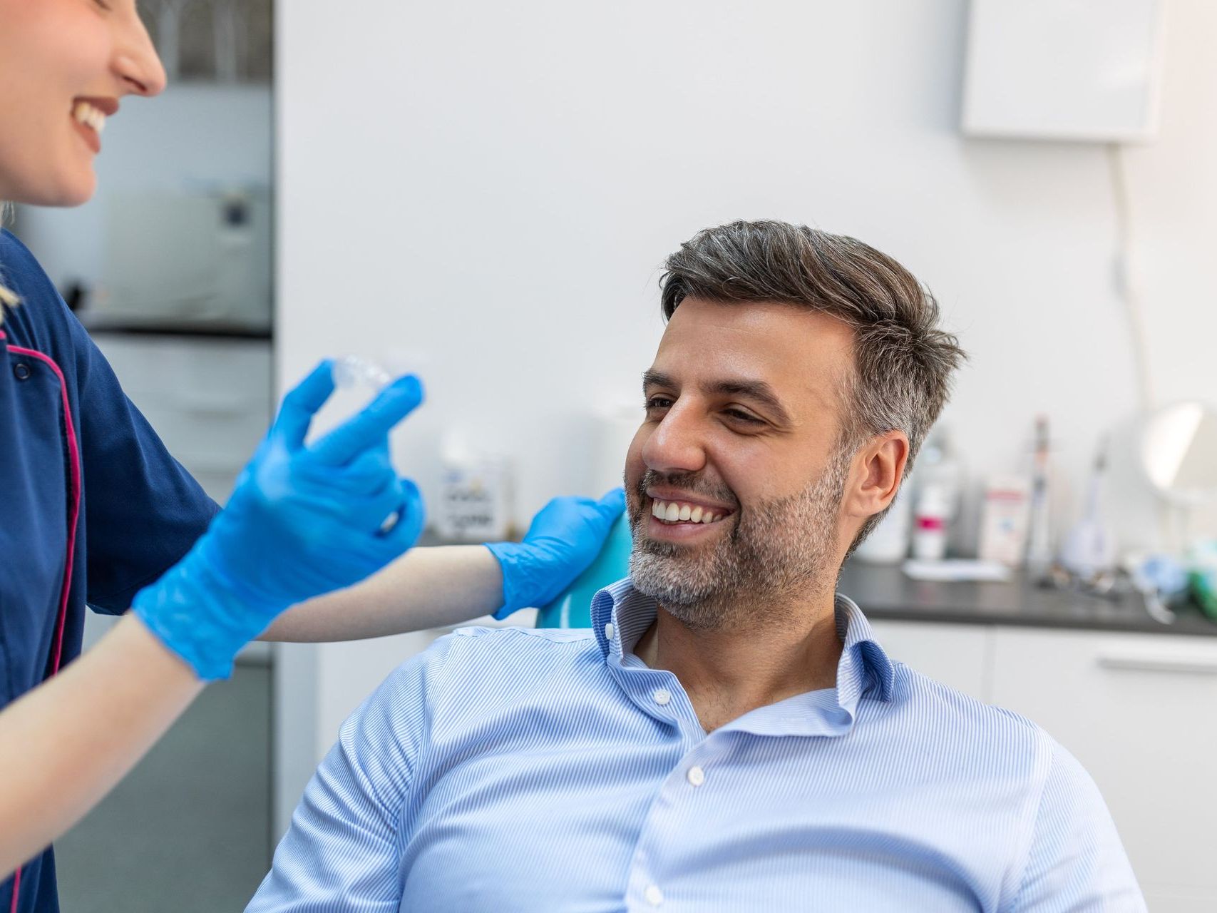 An image of a dental assistant showing a male patient an Invisalign® clear aligners