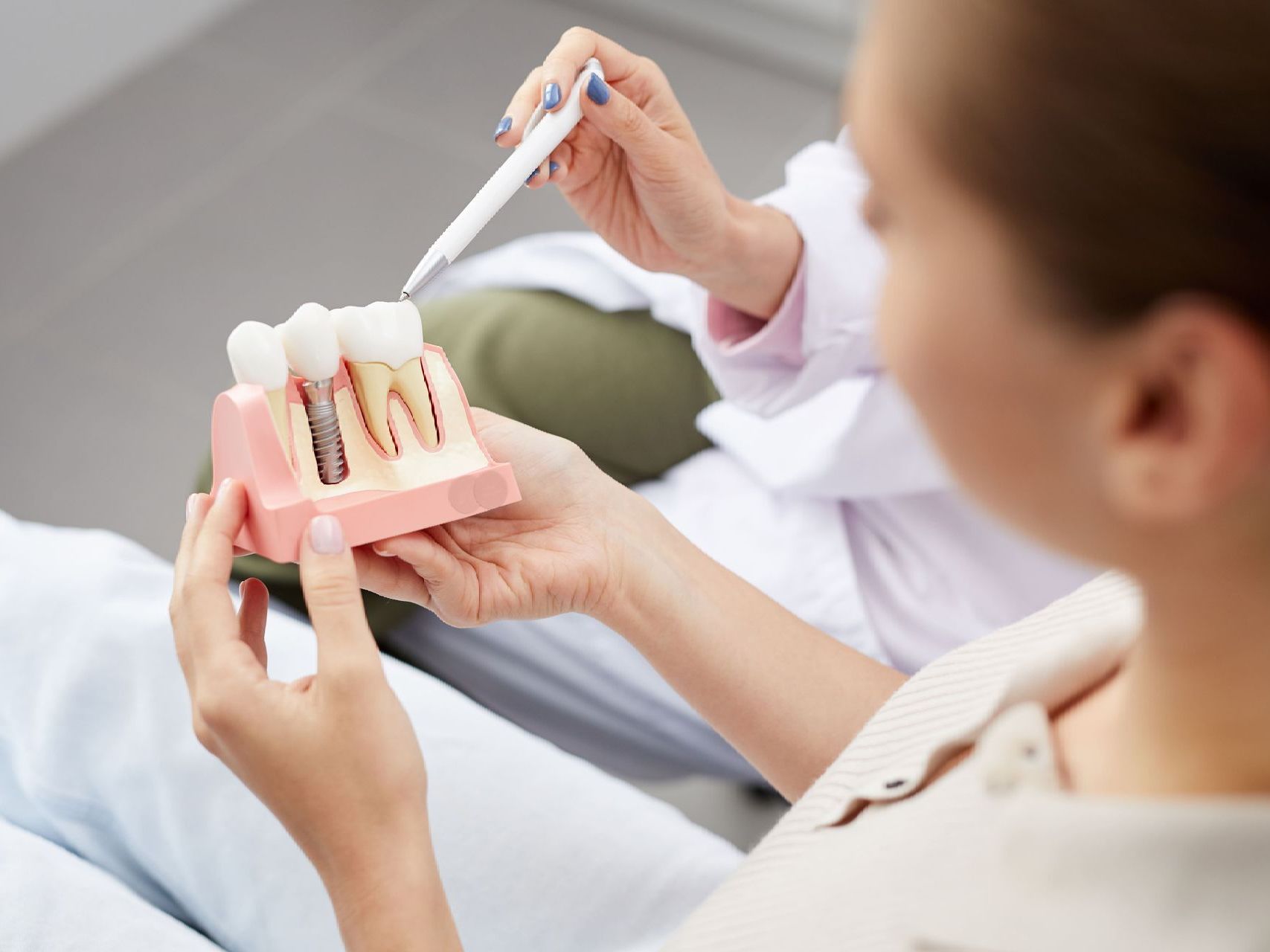 An image of a female patient holding a dental implant model while a dentist explains the model