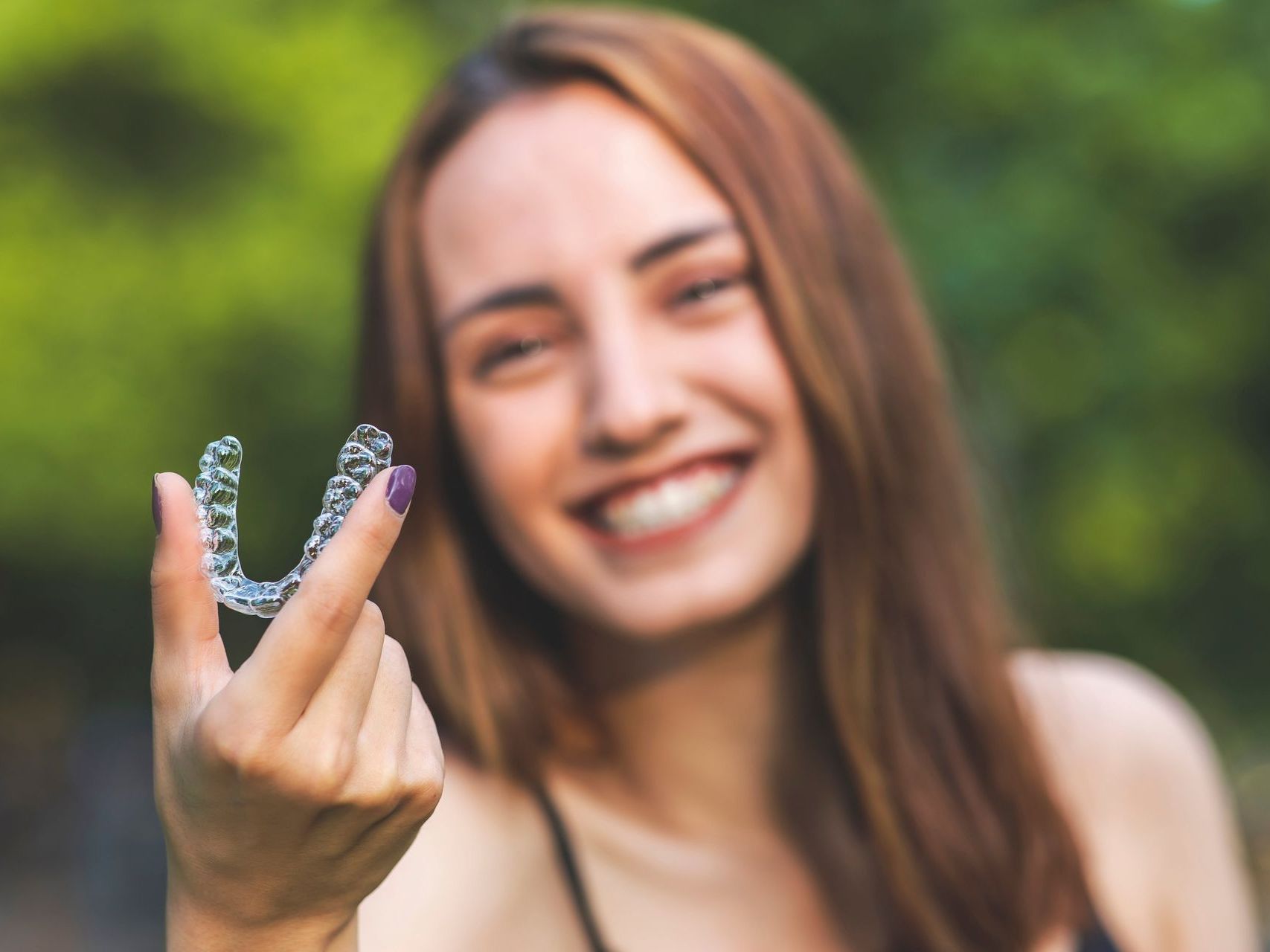 An image of a young woman smiling and holding an Invisalign® clear aligners