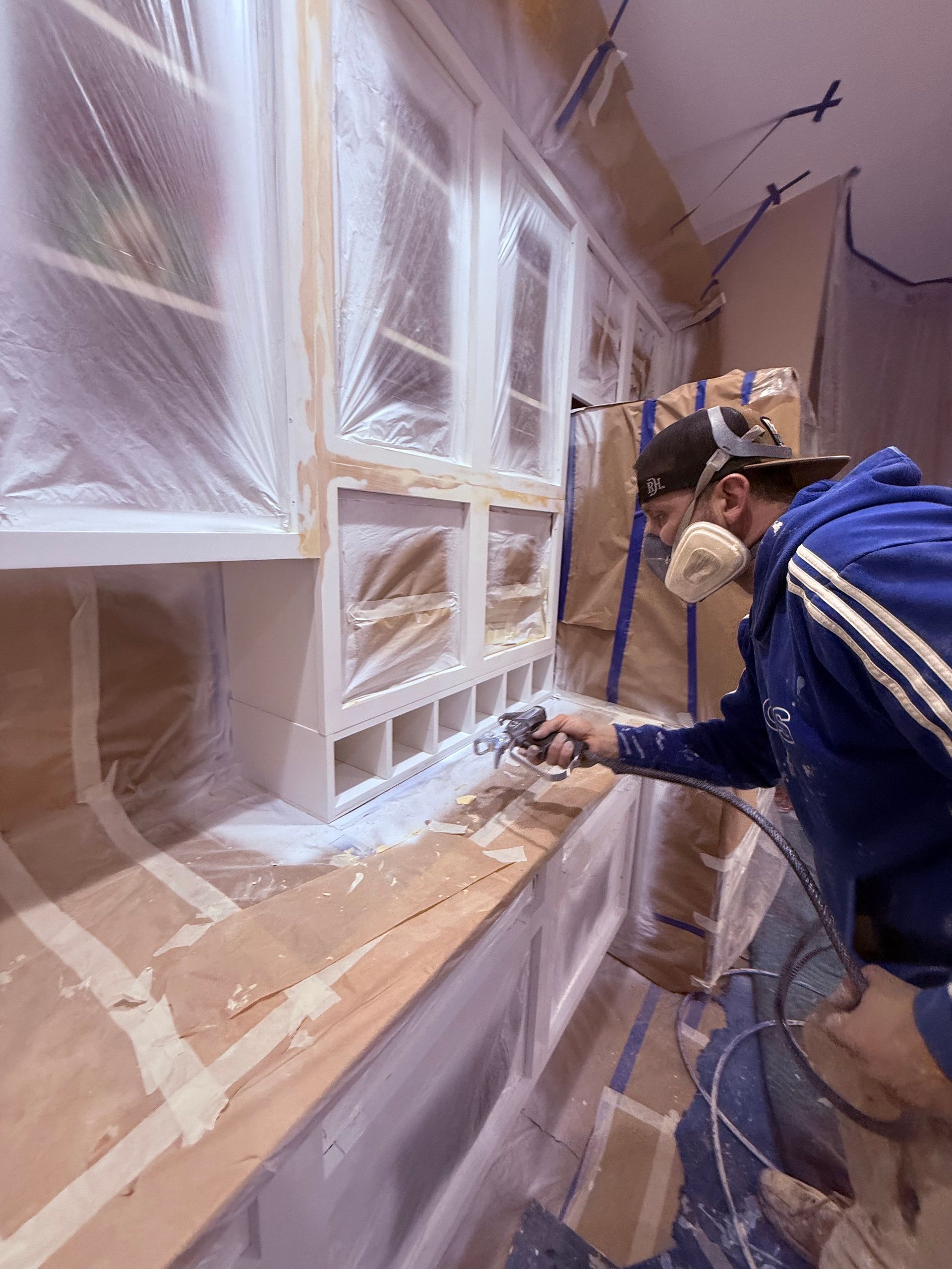 A man wearing a mask is painting cabinets in a kitchen.
