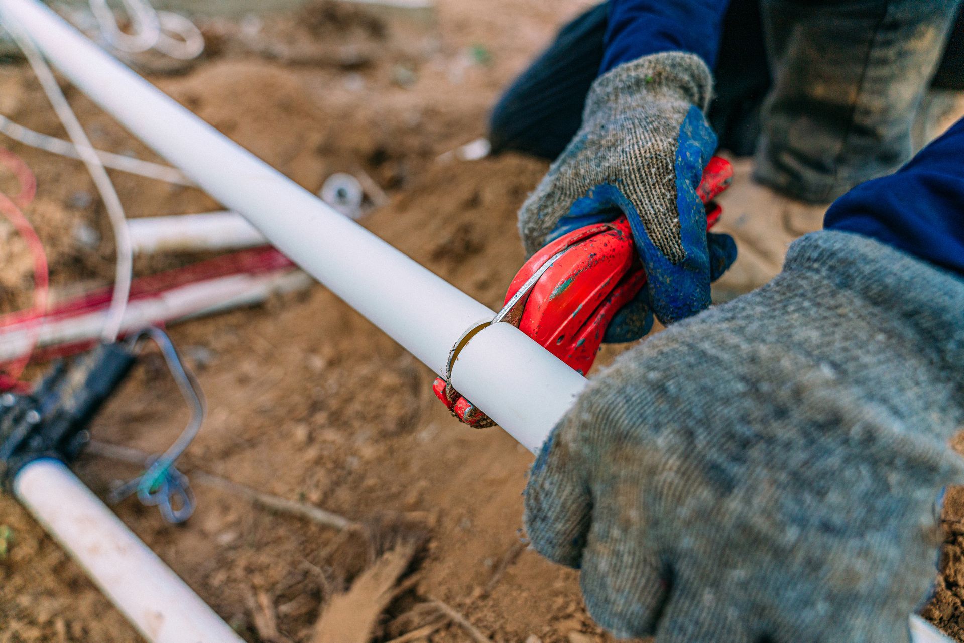 A person is cutting a plastic pipe with a pipe cutter.