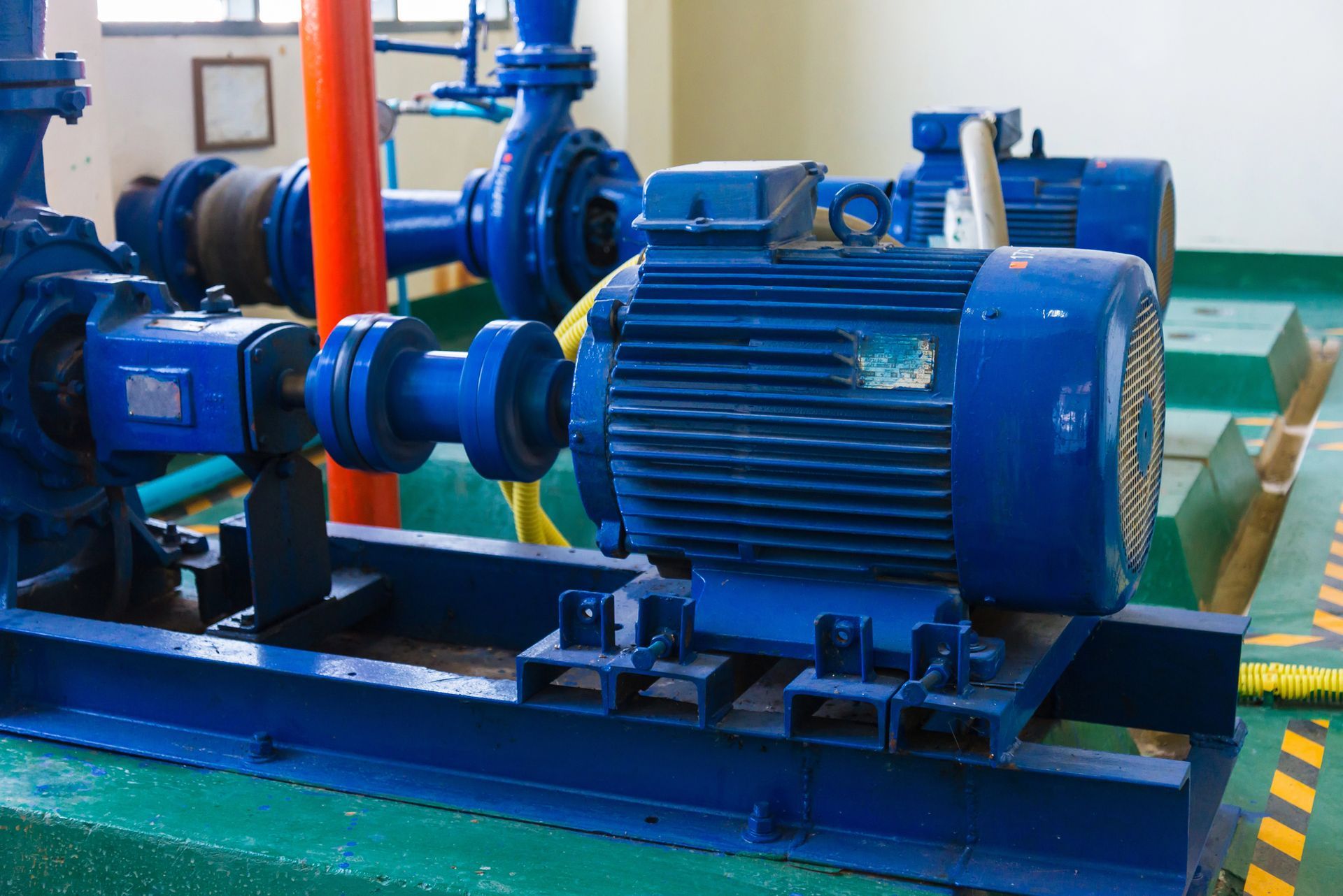 Conjunto de motor y bomba industrial azul montado sobre una plataforma en el suelo de la fábrica.