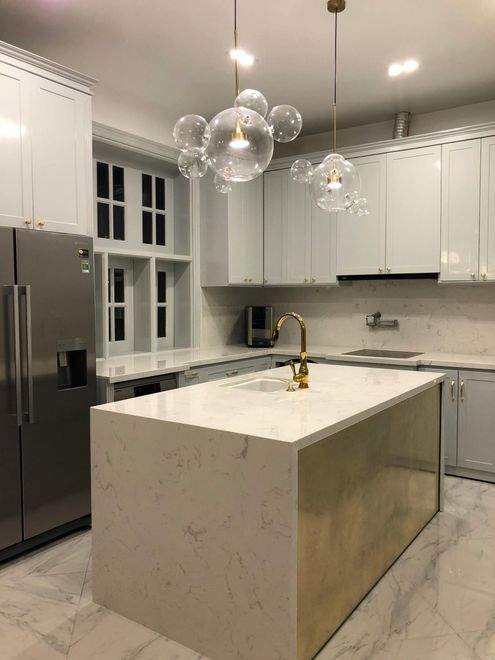 Modern white kitchen with island, marble countertops, and gold accents.