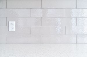 White tiled backsplash with an electrical outlet and a speckled countertop.