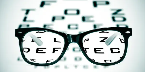 Glasses in front of an eye chart. The letters on the chart are visible through the lenses.
