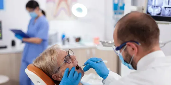 Dentist examining patient's teeth in a dental clinic. Nurse in background.