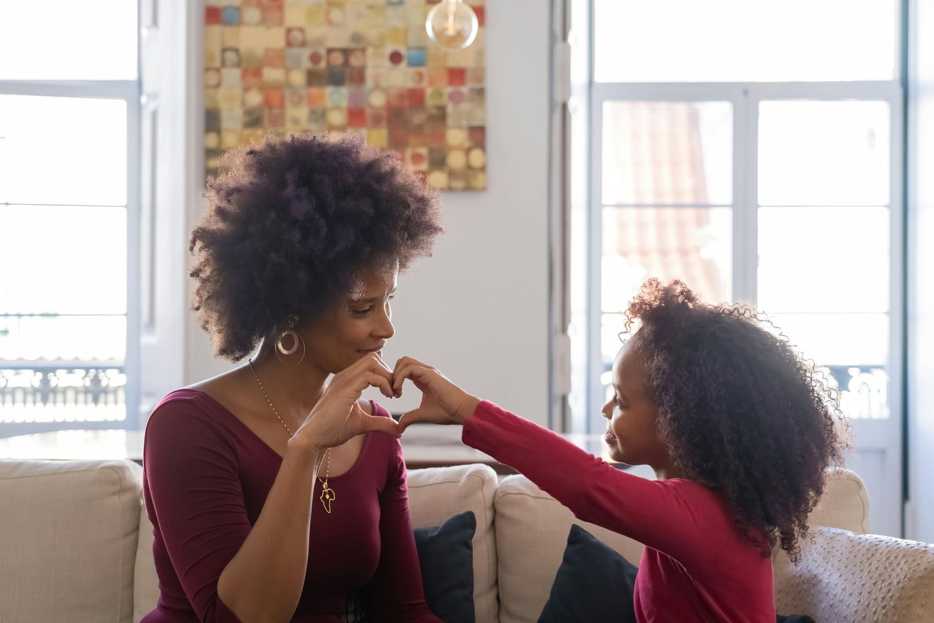 A mother and daughter are making a heart shape with their hands.