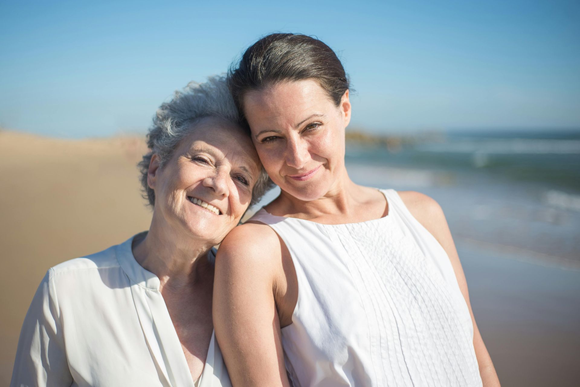 Two women are posing for a picture on the beach.