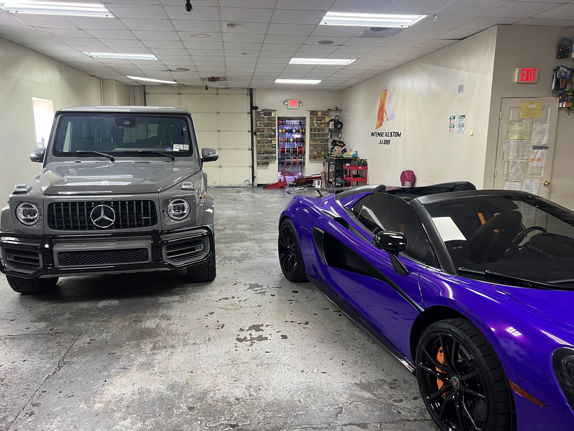Gray Mercedes-Benz G-Class and purple McLaren convertible parked inside a garage.
