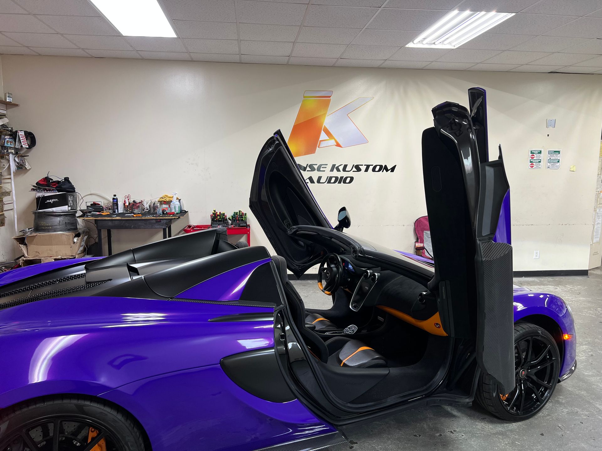 Purple McLaren with doors open, parked inside. Garage background.