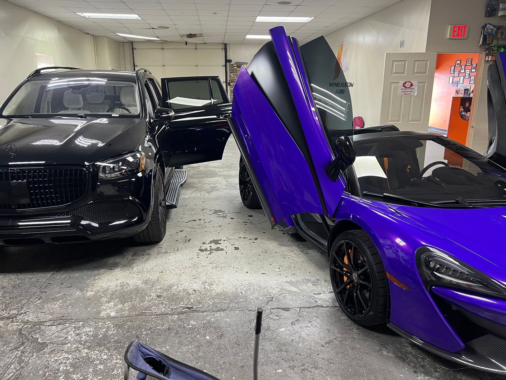 Black SUV and purple sports car with open doors in a shop.