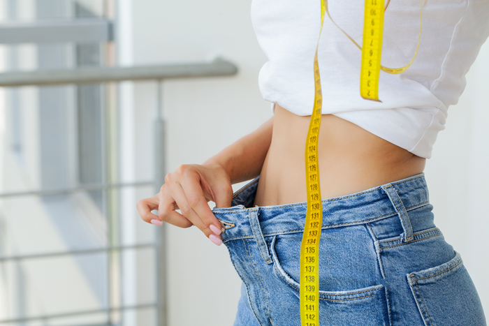 A woman is measuring her waist with a tape measure.