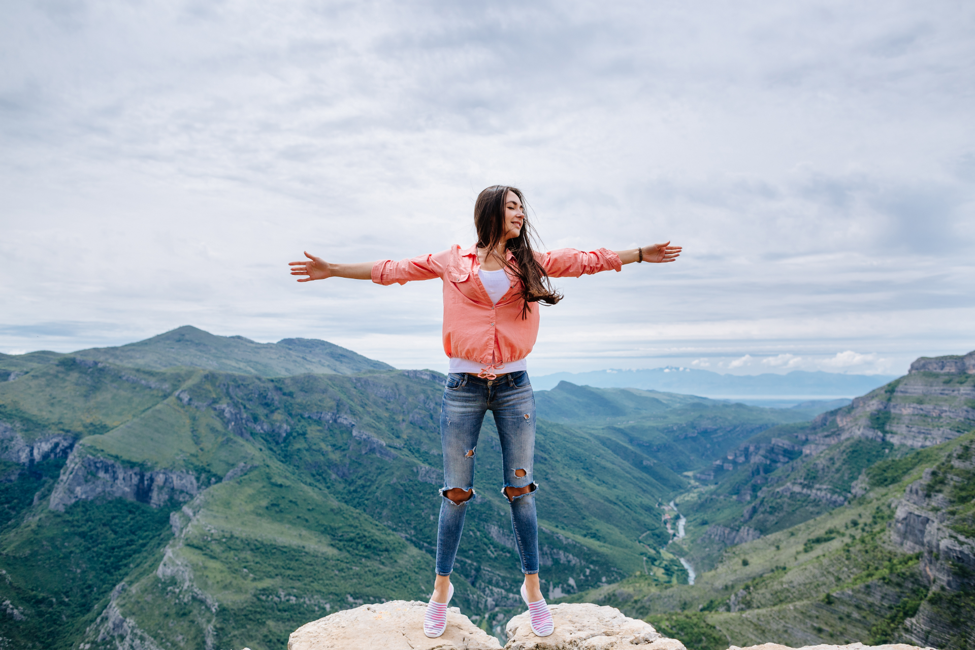 A woman is standing on top of a mountain with her arms outstretched.