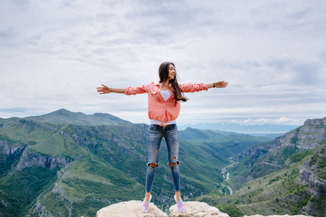 A woman is standing on top of a mountain with her arms outstretched.