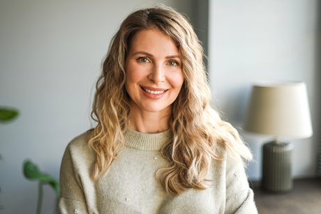 A woman in a sweater is smiling for the camera in a living room.