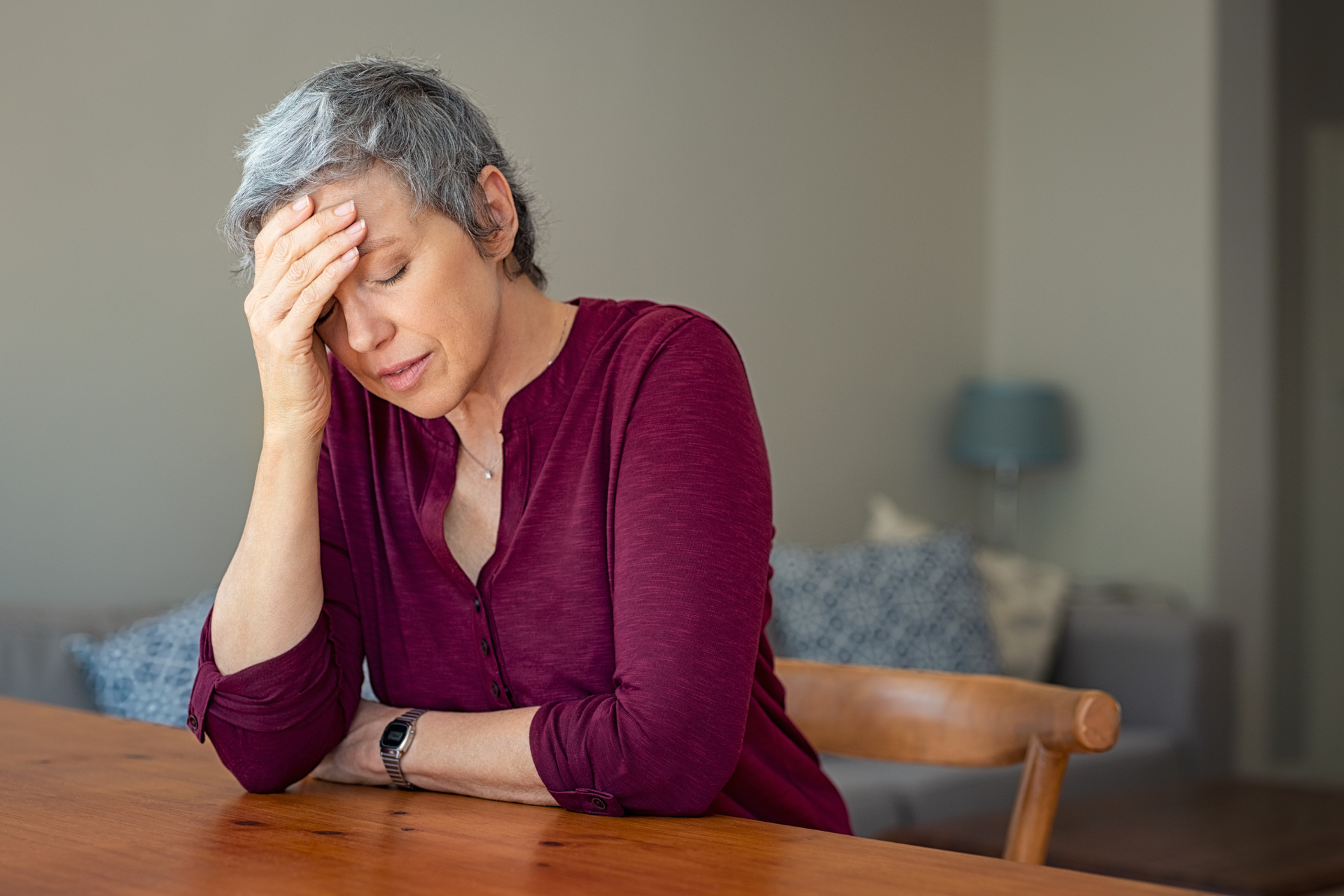 A woman is sitting at a table with her hand on her forehead.