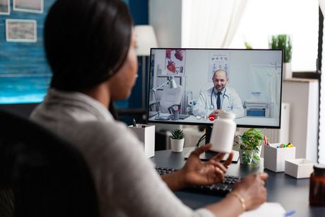 A woman is holding a bottle of pills while talking to a doctor on a video call.