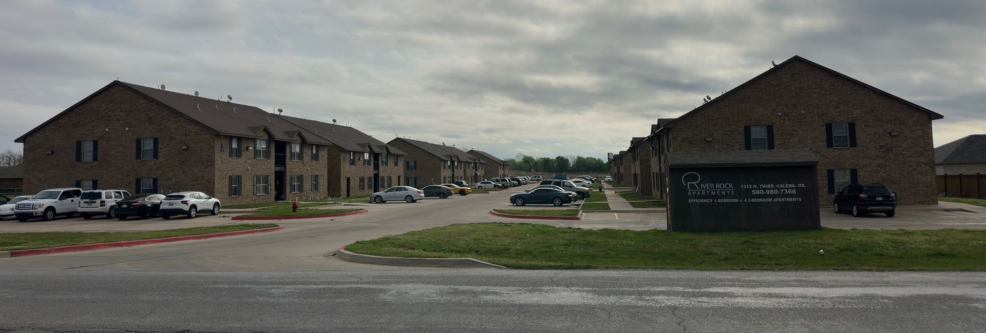 River Rock Complex - A row of brick houses with cars parked in front of them on a cloudy day.