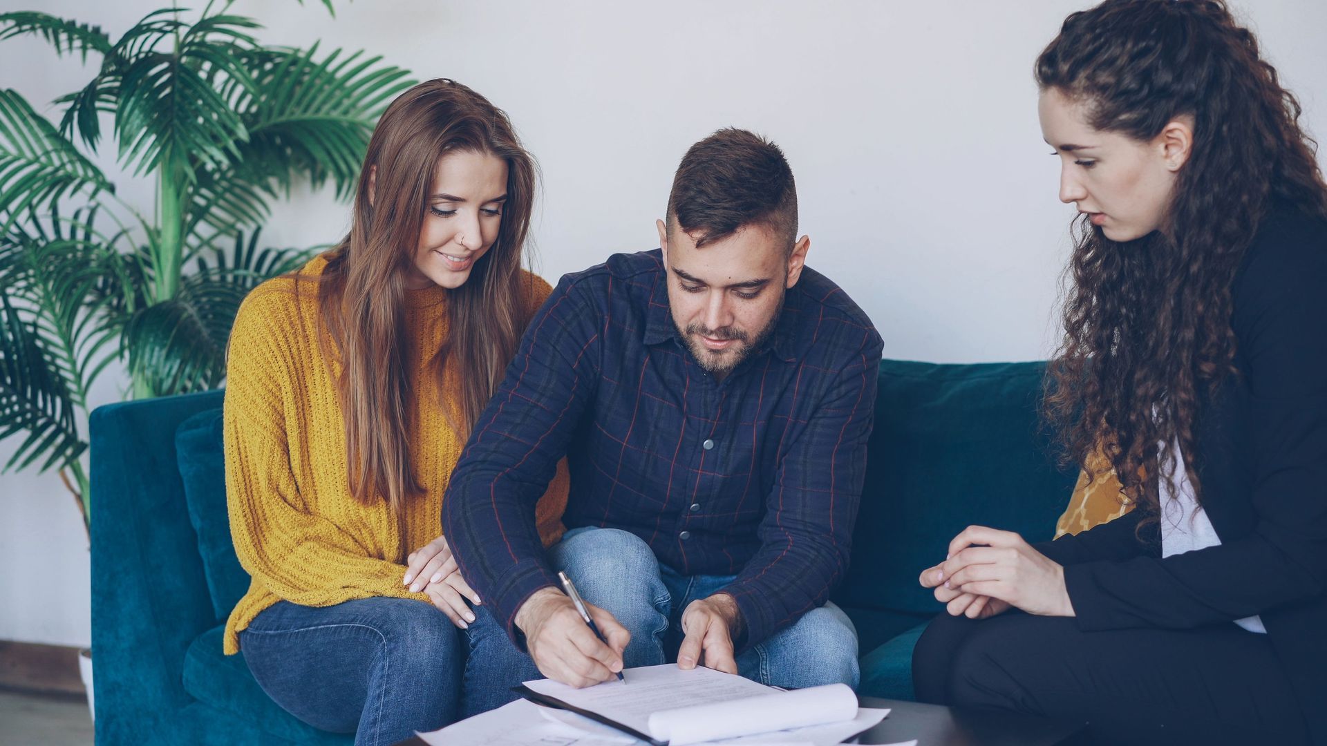 Three people on a couch reviewing documents in a living room with a plant nearby.