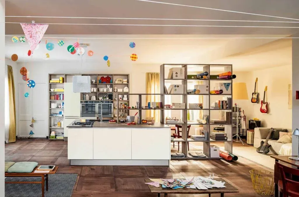Open-plan kitchen with shelving, counter, and colorful decorations. Guitars and seating in the background.