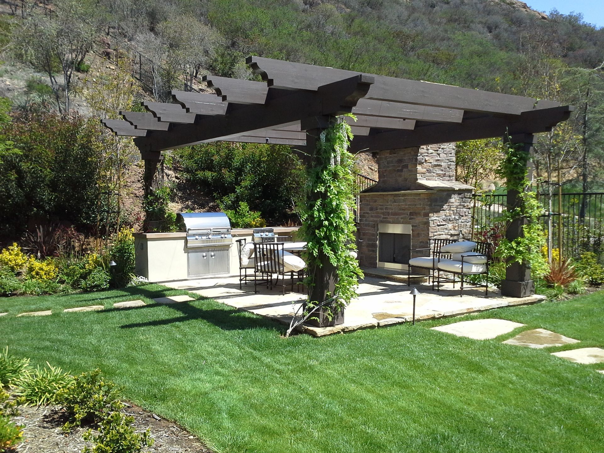 A patio with a grill and a fireplace under a pergola