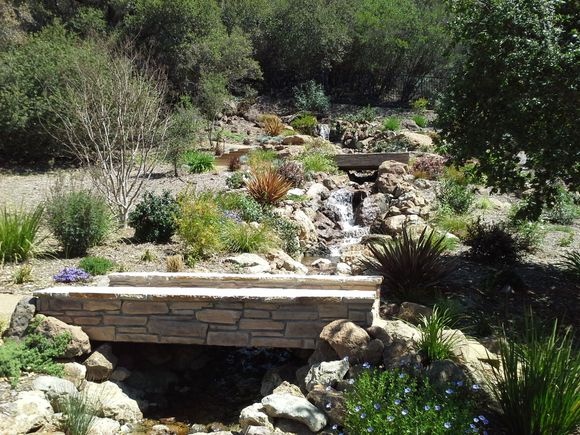 A stone bridge over a stream with a waterfall in the background