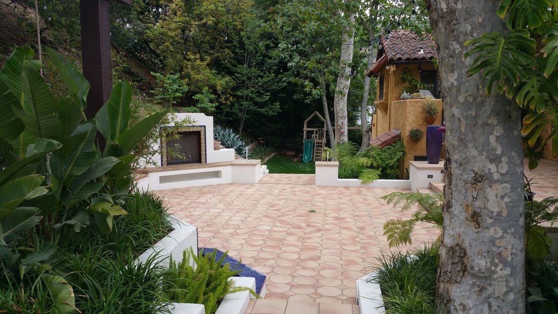 A brick walkway leading to a wooden house surrounded by trees and bushes.