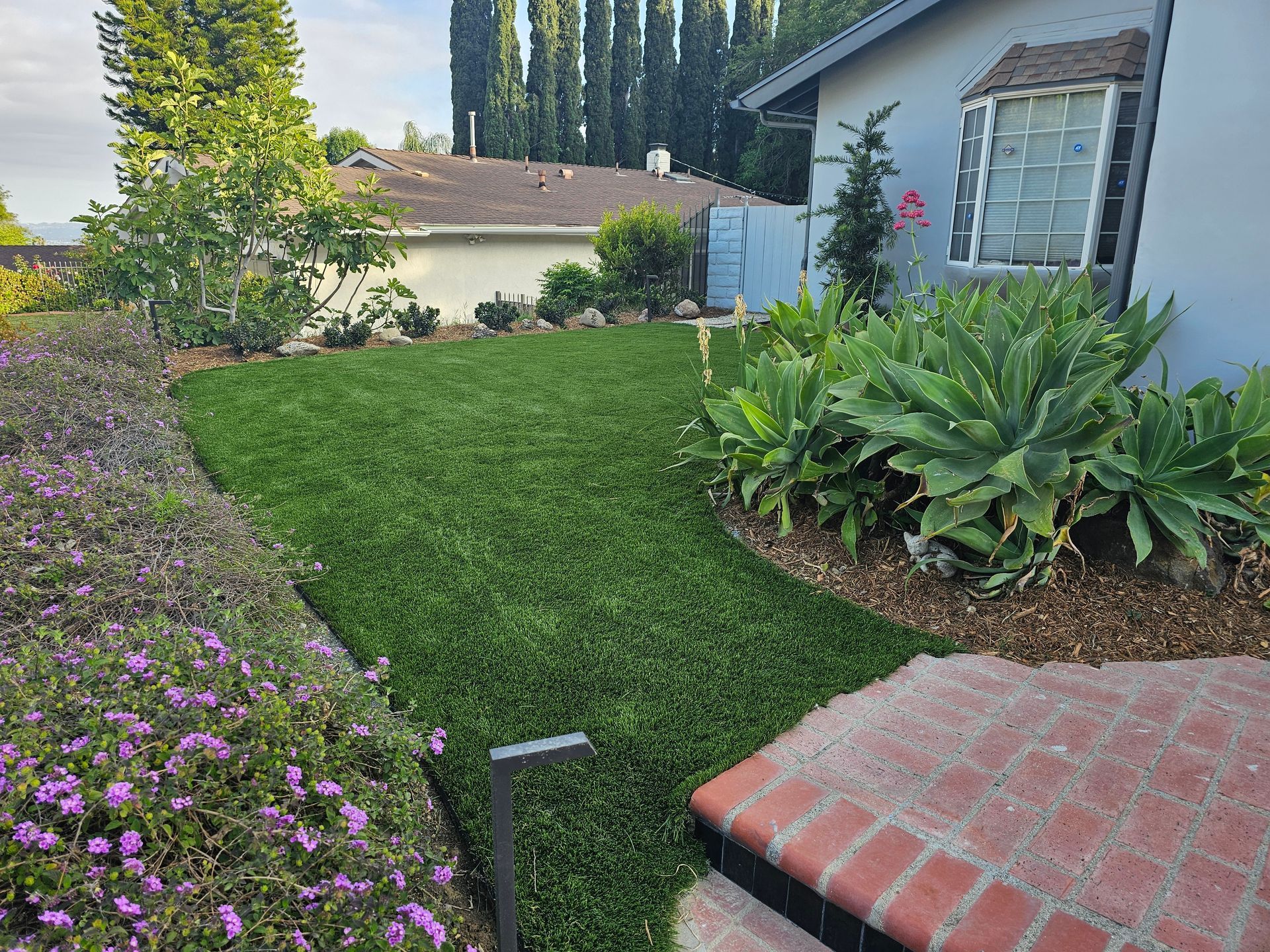 A house with a lush green lawn and purple flowers in front of it.